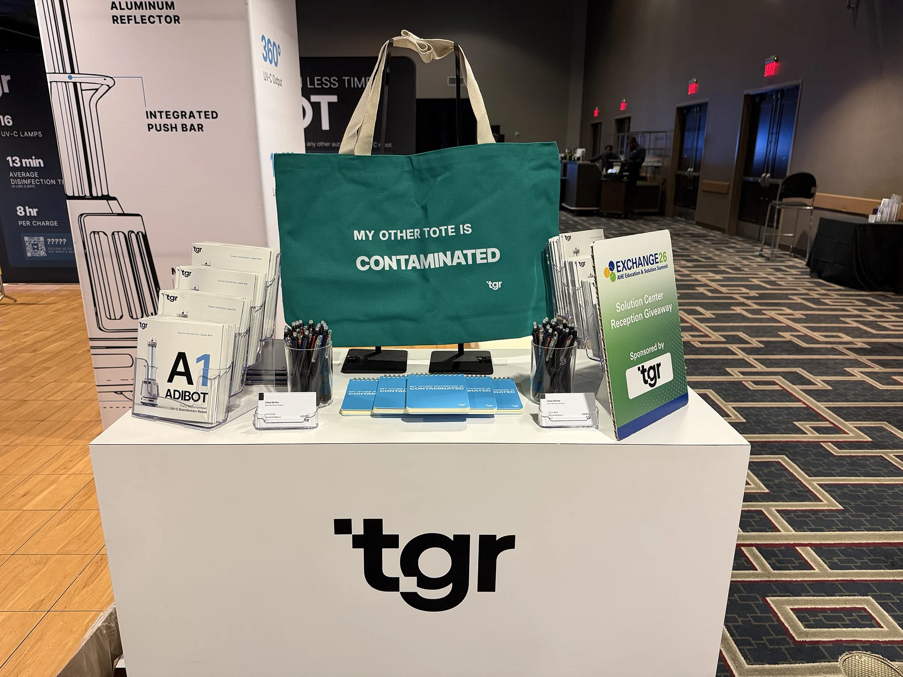 AHE Exchange26 上的 TGR 展台，摆放着宣传册、胸卡卷轴和绿色手提袋。