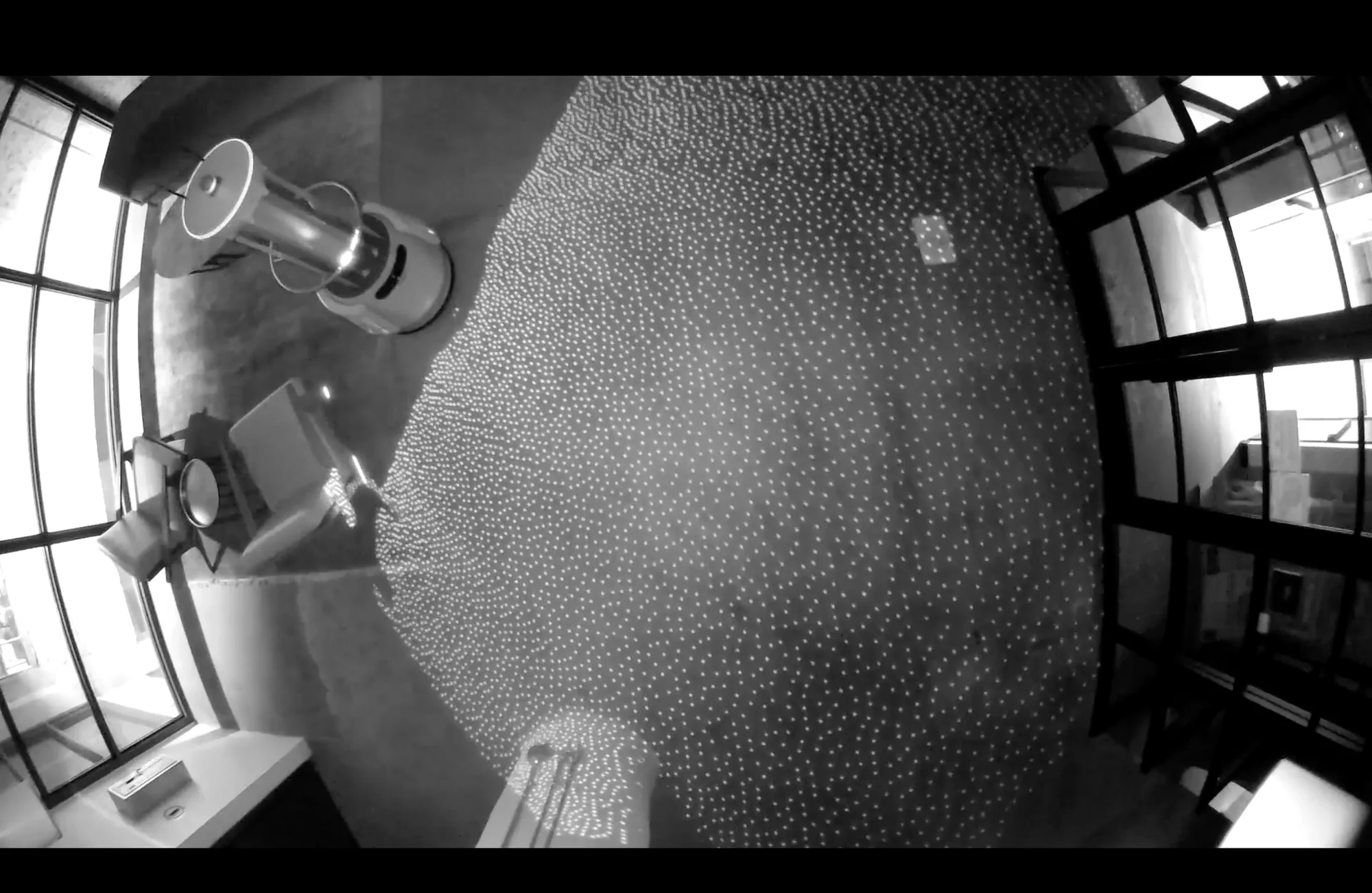 Greyscale fisheye view from a robot’s depth camera, showing the projected infrared dot pattern spread across a room floor.