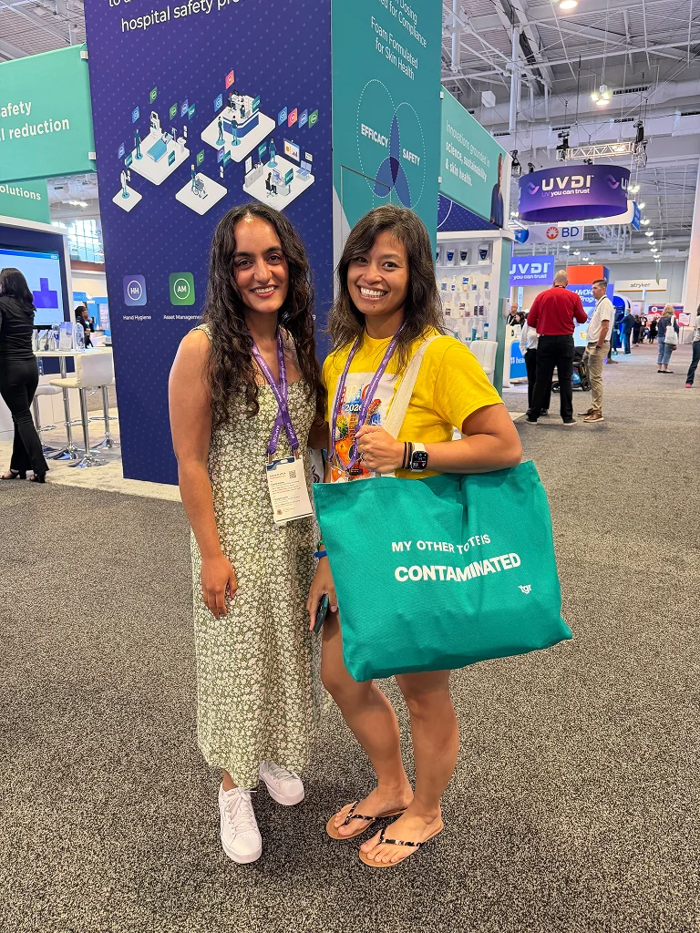 Two attendees posing at the TGR booth, one holding a green TGR tote bag.