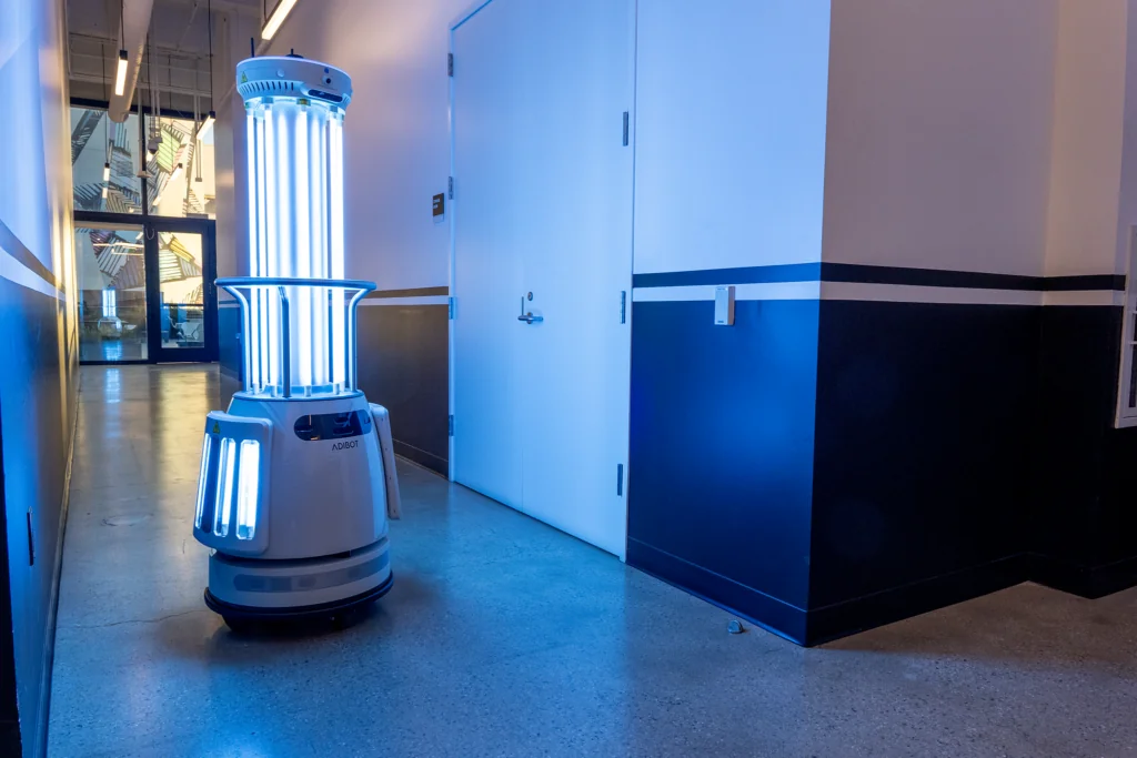 A1 robot with illuminated vertical UV-C lamps beside a doorway.