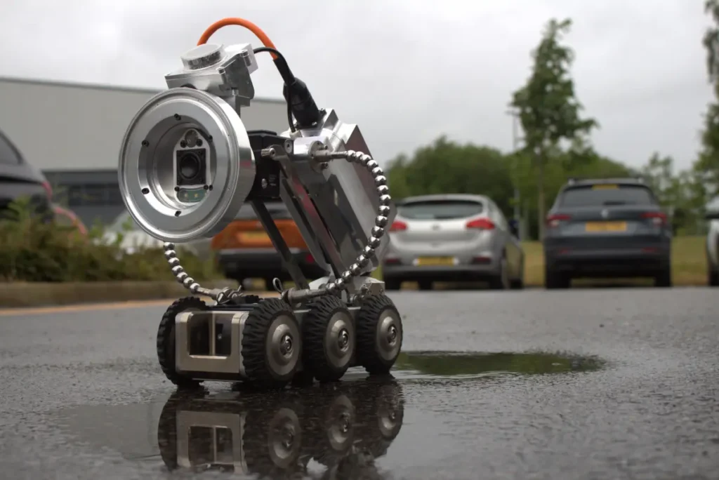 PipeBot inspection robot with a forward-facing camera and six wheels on wet pavement.