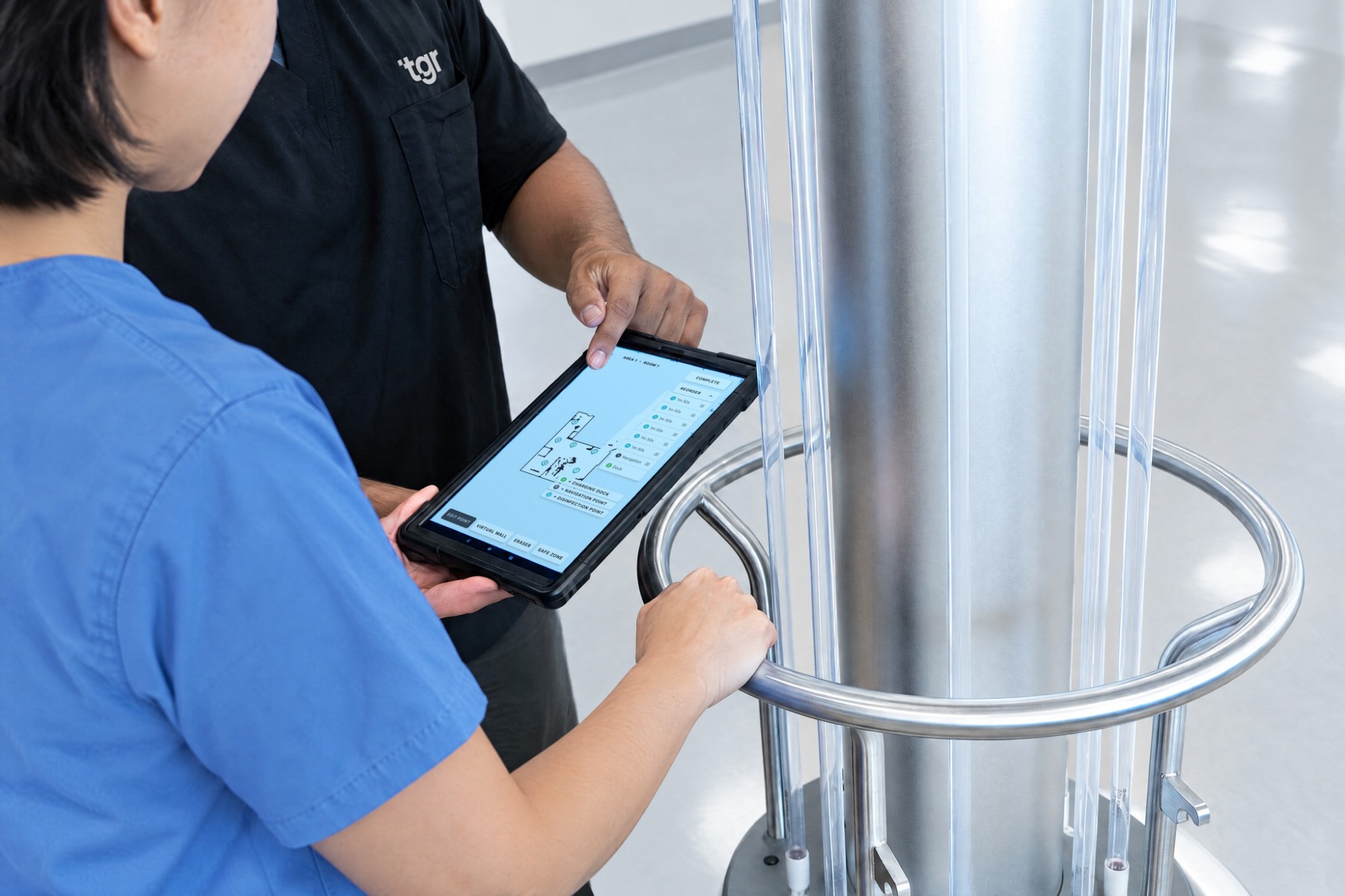 A TGR team member points out a disinfection point on the A1 tablet’s room map while an operator holds it beside the robot, UV-C lamps off